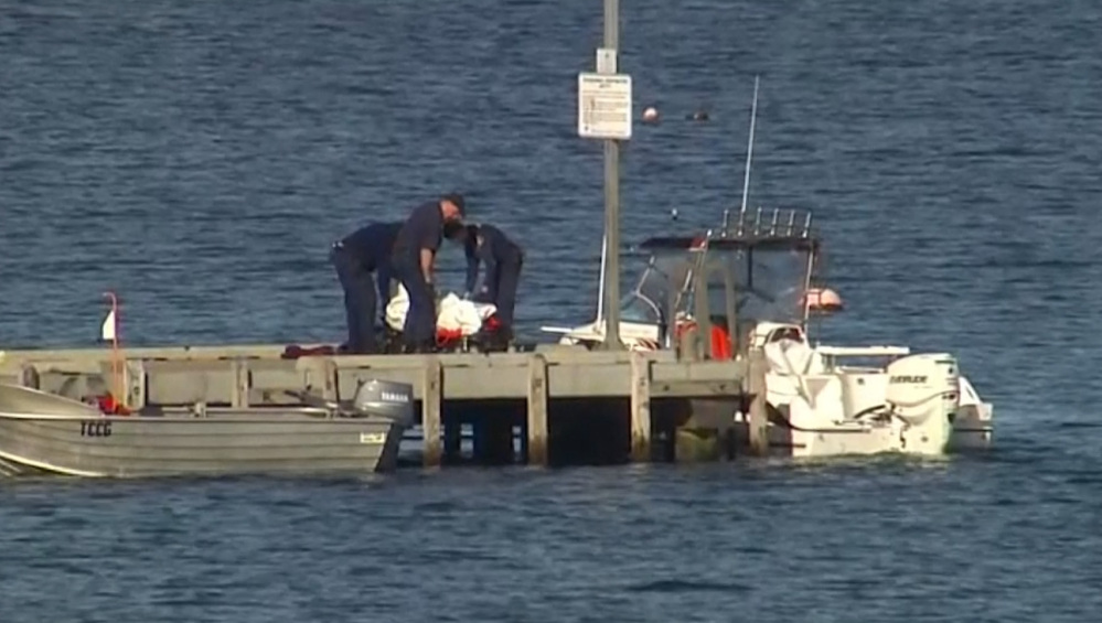 In this image taken from video, police carry a body in a bag and place it in on a stretcher on a jetty in Triabunna, off the Australian island state of Tasmania, on Saturday.
