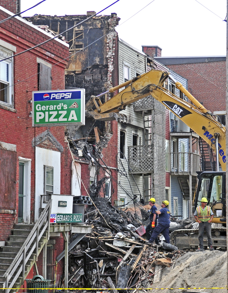 Officials, with the help from an excavator, investigate the scene the morning after a major fire in downtown Gardiner.