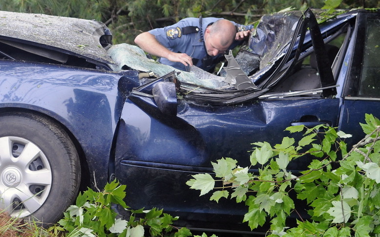 State Trooper Kyle Pelletier searches the interior of a car that struck a tree, killing the operator, on the Plains Road in Litchfield on Sunday.