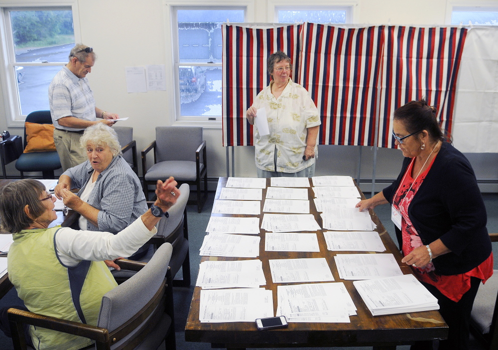 Dian White, left, directs Beverly Chase, second from right, to a ballot box Tuesday in Litchfield as Chase’s husband, Daniel, prepares to vote after being issued a ballot by Esther Slattery, second from left. Litchfield, Wales and Sabattus residents were voting on the Regional School Unit 4 school budget.