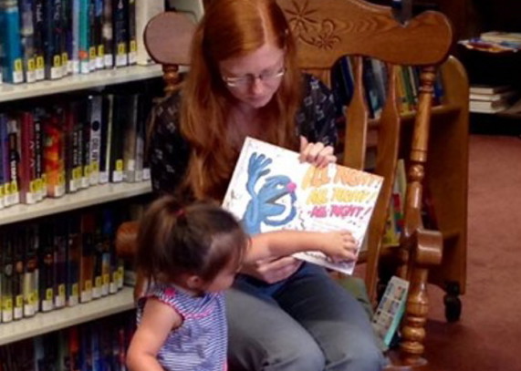 Skowhegan Town Manager Christine Almand, sitting, shares a favorite  story at the Skowhegan Free Public Library while Zoeymarie Rinaldi lends a hand by turning the pages.