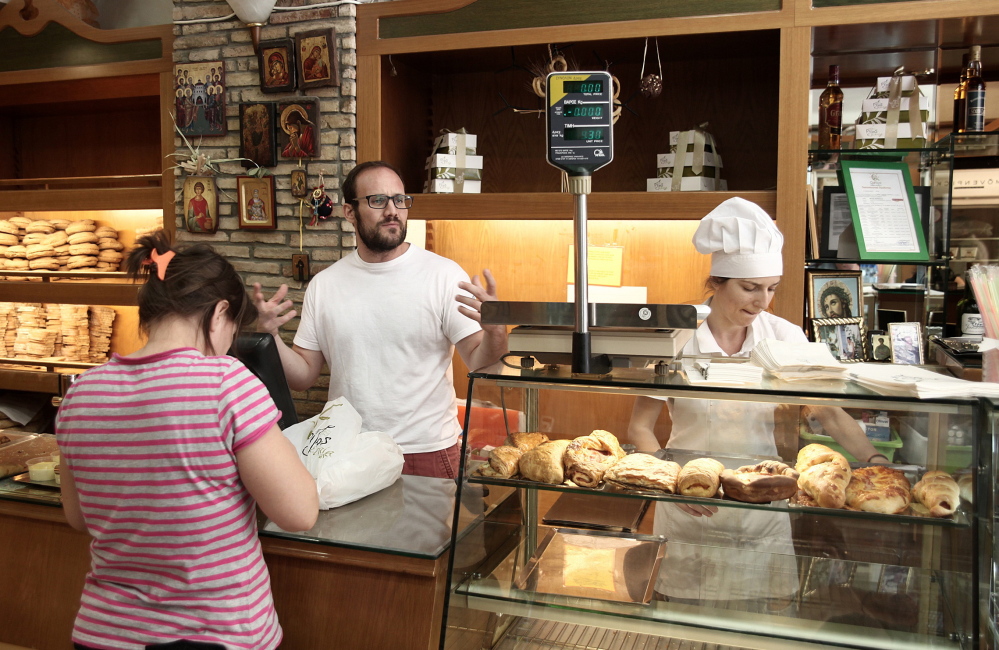 Alexandros Rizos, center, works at his bakery in Athens on Monday. Under terms of the new agreement, it’s almost certain Greece’s sales tax on food will rise from 13 percent to 23 percent, meaning Rizos will have to raise prices for customers.