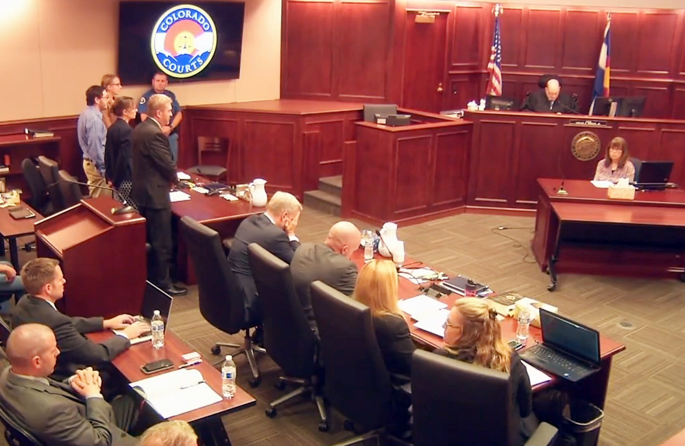 In this image taken from video, James Holmes, standing on the far left, listens as the guilty verdicts against him are read Thursday. Holmes was found guilty of murder in the deaths of 12 people in July 2012. In the center, lead prosecutor George Brauchler puts his hands up to his face as the verdicts are read.