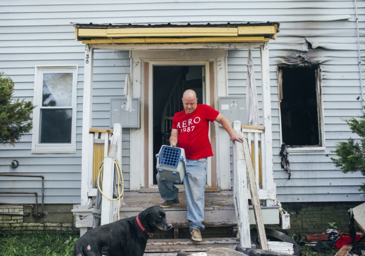 Jason Meyer, with his dog Brooklyn, carries his cat, Kitty, out of his apartment at 135 Bridge St., after a fire overnight displaced residents in Westbrook on Monday. Meyer hadn’t seen the cat since the fire started, but Brooklyn found Kitty safe in a closet.