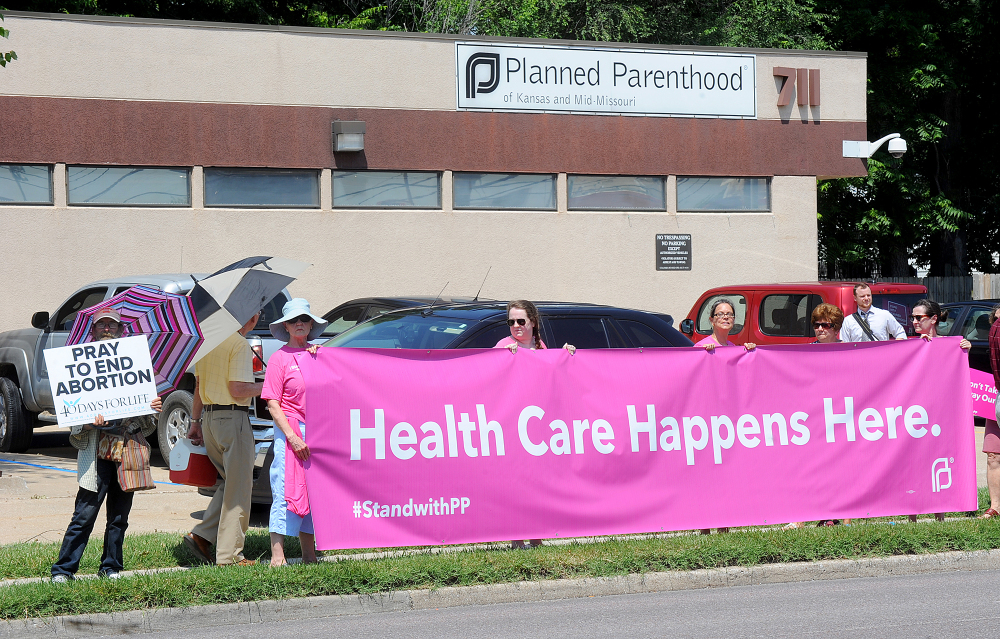 A man holding a sign stands next to five women holding a large banner supporting Planned Parenthood of Kansas and Mid-Missouri on Tuesday in front of Planned Parenthood in Columbia, Mo. 
The Associated Press