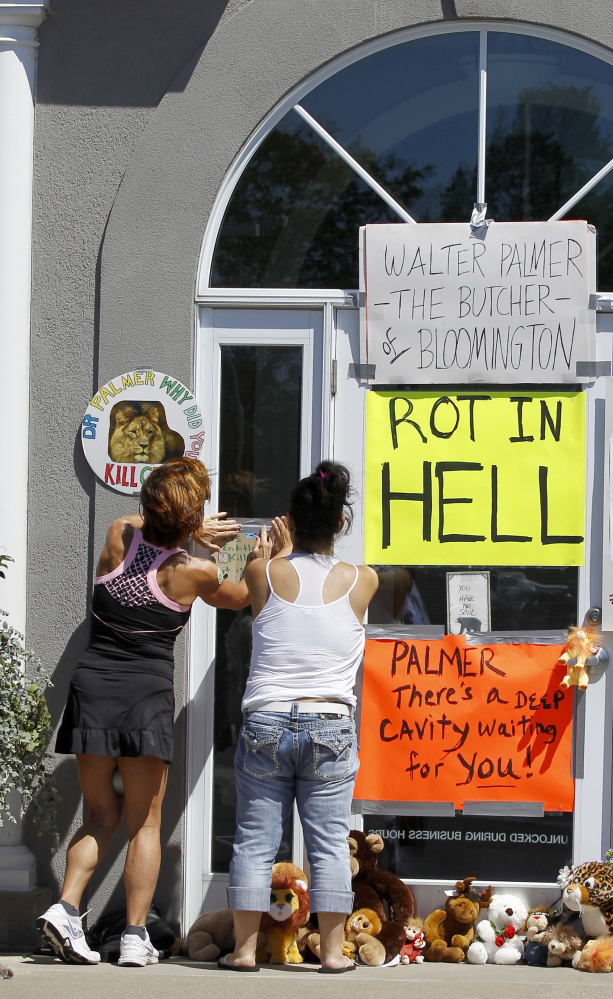 Women add signs to the door outside Dr. Walter James Palmer’s dental office in Bloomington, Minn., on Wednesday. Palmer’s killing of a protected lion just outside Hwange National Park in Zimbabwe had led to calls for an end to trophy hunting.