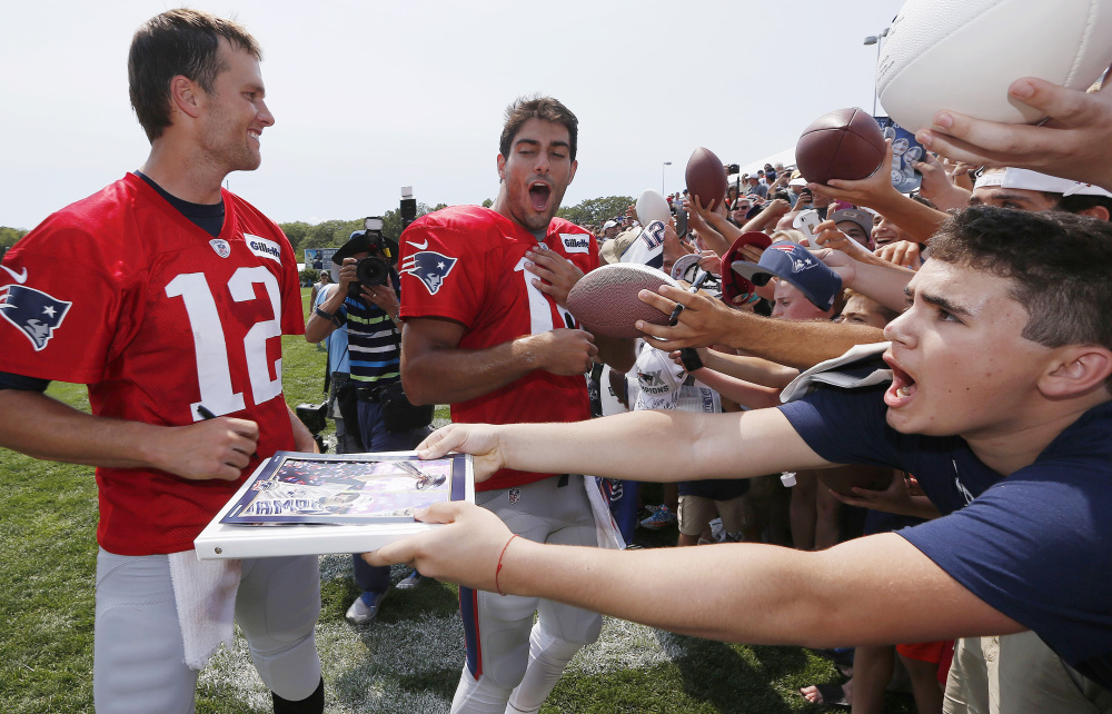 New England Patriots quarterbacks Tom Brady (12) and Jimmy Garoppolo, center, sign autographs during training camp Saturday in Foxborough, Mass.