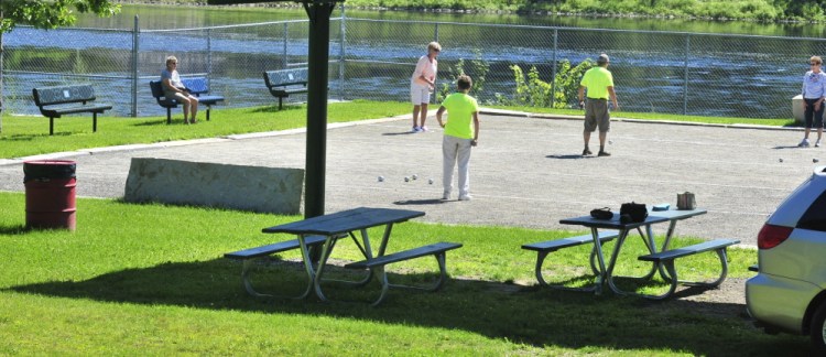 People play petanque Saturday at Mill Park in Augusta. The city is considering replacing the high chain-link fence behind them with a shorter one and building a mile-long looped walking path around the park’s perimeter, affording views of the Kennebec River.