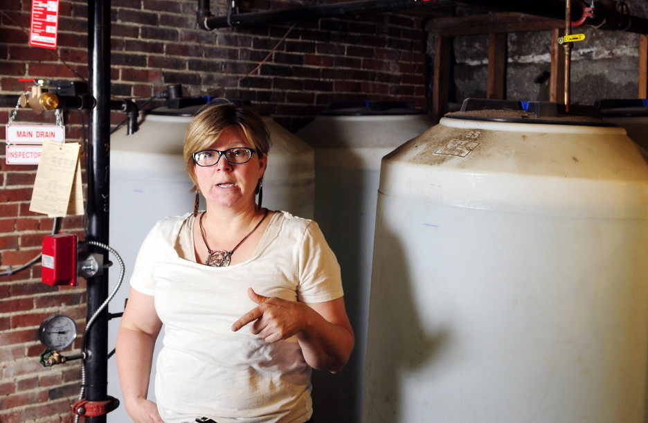 Standing beside water tanks in the basement, Clare Marron talks about the sprinkler system in her Water Street building that contains Monkitree gallery and her apartment on July 23 in Gardiner. Hallowell officials were scheduled to discuss sprinkler systems on Monday night.