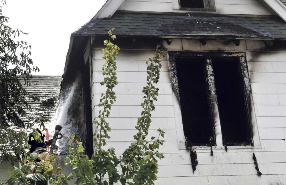 Waterville firefighter Richard Haviland sprays water through a window into the heavily damaged second floor of a home on Silver Street in Waterville on July 29. Officials still haven’t determined the cause of the fire.
