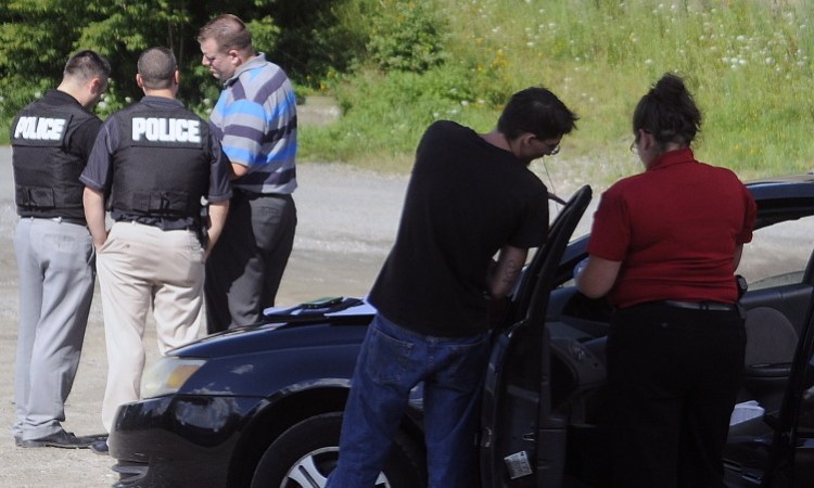 Augusta police detectives confer Thursday under Memorial Bridge in Augusta while searching a vehicle following a robbery at the Big Apple store on Stone Street.