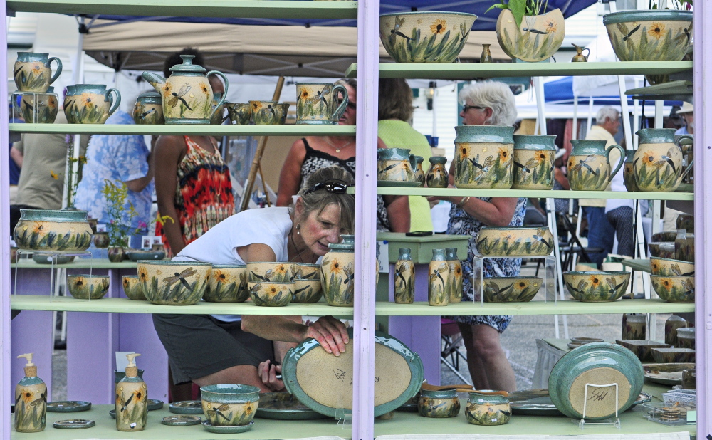 Sue Firlotte, of North Monmouth, picks up a platter on Saturday in The Potter’s House booth during the Winthrop Summer Festival in downtown Winthrop.