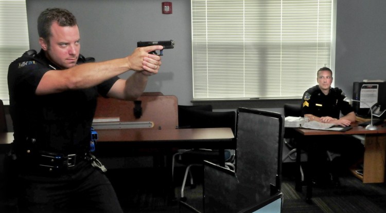 Waterville police officer Damon Lefferts, left, takes aim with a simulator pistol at a projected image of a criminal as Sgt. Lincoln Ryder operates software for a laser shot training system on Wednesday.