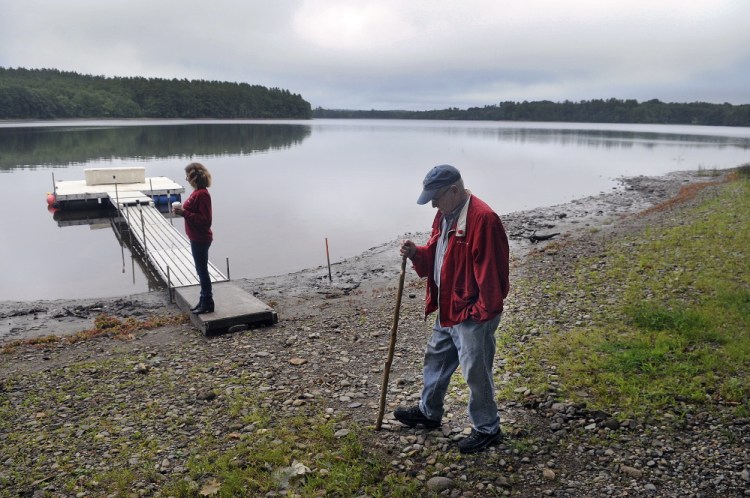 Stan Whittier walks on the shore of Clary Lake in Jefferson earlier this month while his daughter, Jane Roy, stands on the family’s dock. It’s been nearly three years since property owners around the lake in Jefferson and Whitefield appealed to the state to intervene over a low water level, and residents say the situation still hasn’t improved.