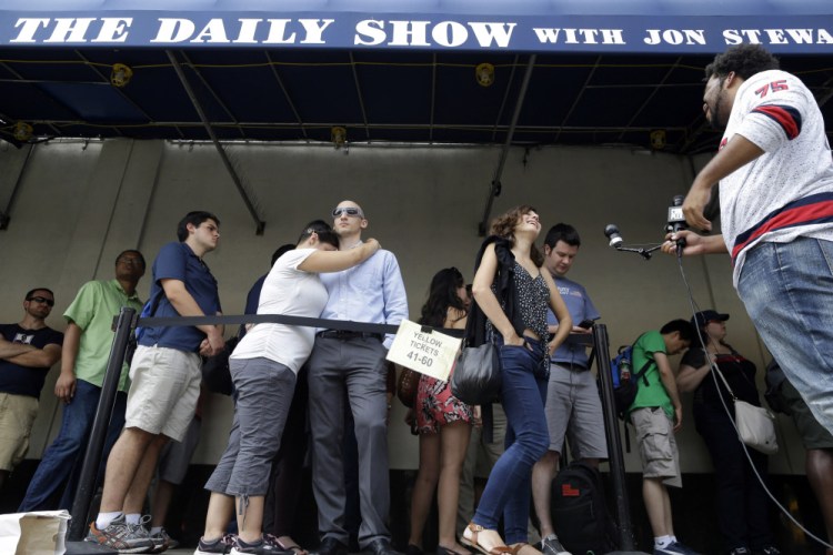 Alexandra Mele, second from right, is interviewed and Ariana and Isaac Levin embrace as they wait in line to enter for the final taping of  “The Daily Show with Jon Stewart” on Thursday in New York. Stewart said goodbye Thursday after 16 years on the show that established him as America’s foremost satirist of politicians and the media.