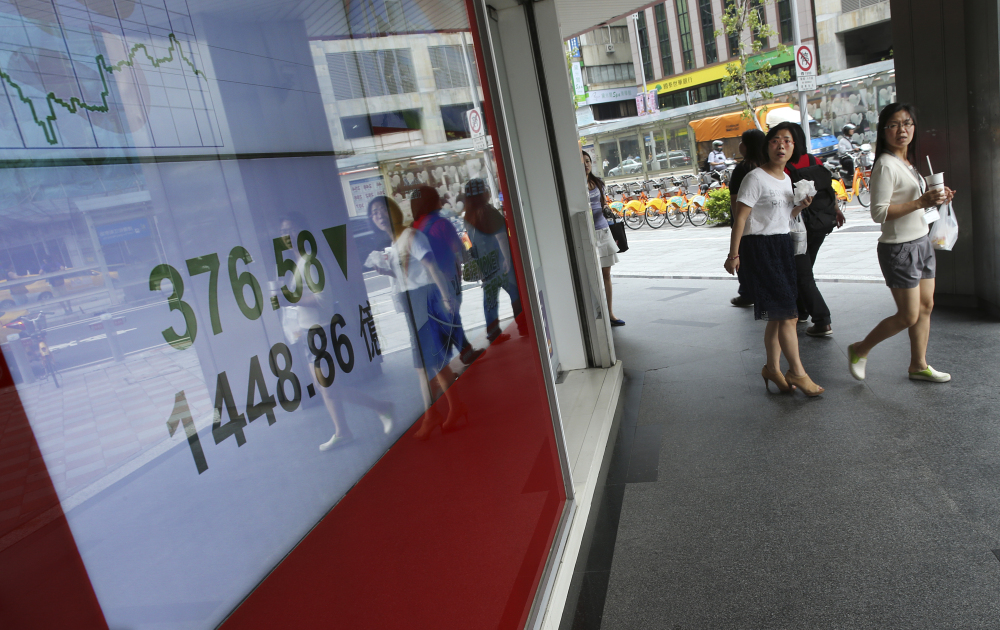 Office workers pass by monitors displaying the Taiwan Stock Exchange in Taipei on Monday. Stocks tumbled across Asia, with China’s main index losing more than 8 percent as investors, shaken by the sell-off last week on Wall Street, unloaded shares in practically every sector.