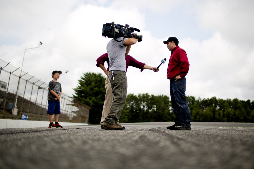 Travis Benjamin of Morrill has been the center of media attention heading into his attempt to win a third straight Oxford 250. His son, Kaiden, 8, watches and listens to a television interview.