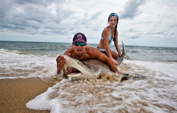 Elliot Sudal catches a brown shark off the beach in Siasconset, on Nantucket. Standish native Marisa Butler helps him measure and tag the sharks before they are released. Boston Globe staff photo by Stan Grossfeld