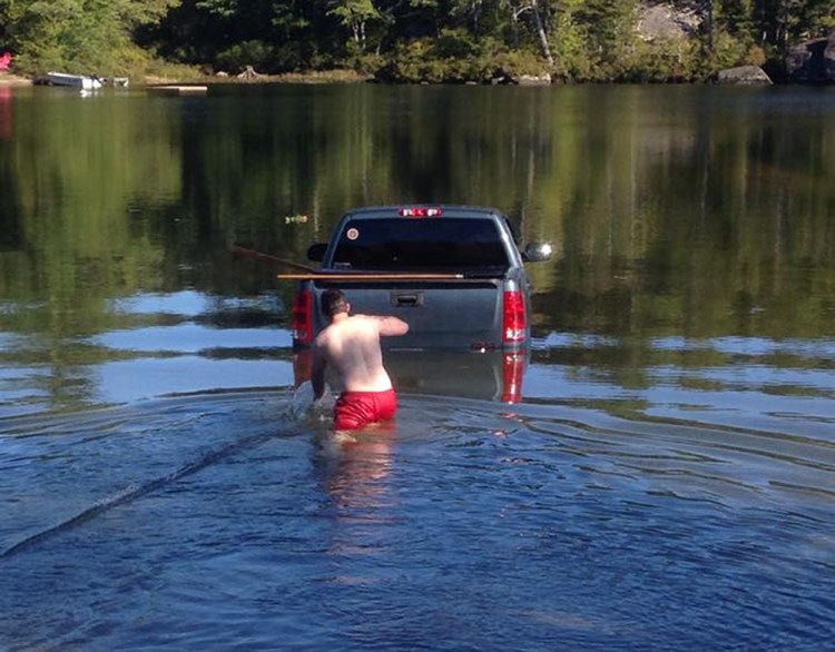 A man wades out to his truck after it rolls into Branch Lake near Ellsworth with his dog inside the cab. 