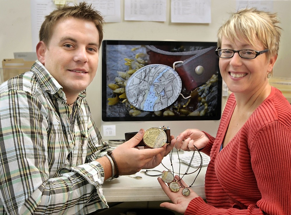 Gordon Chibroski/Staff Photographer
John Guptill and Charlotte Leavitt of Chart Metalworks with some of their jewelry creations fashioned from cutouts of nautical charts.