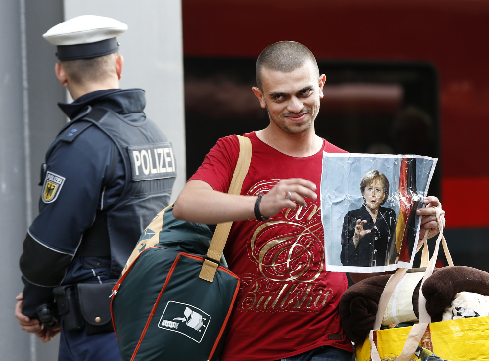 A refugee carries a picture of German Chancellor Angela Merkel as he arrives at the main train station in Munich, Germany, Saturday, Sept. 5. Hundreds of refugees arrived in various trains to get first registration as asylum seekers in Germany.