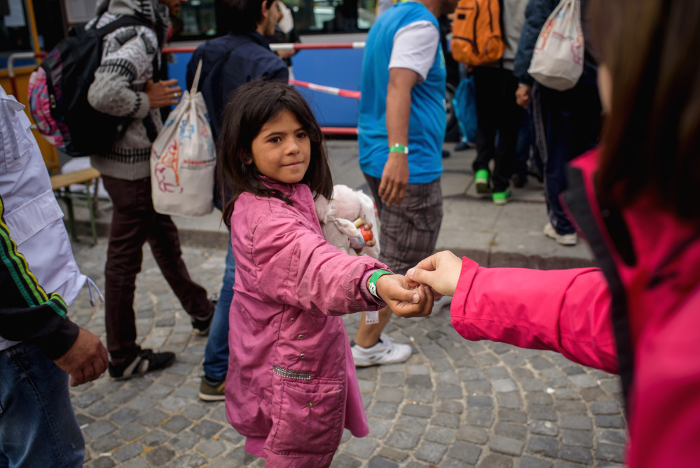 A woman gives some euro coins to a refugee child, who has arrived by train at the central station in Munich, southern Germany on Saturday, Sept. 5. Since Saturday more than 7,000 Arab and Asian asylum seekers surged across Hungary’s western border into Austria and Germany following the latest erratic policy turn by Hungary’s immigrant-averse government.