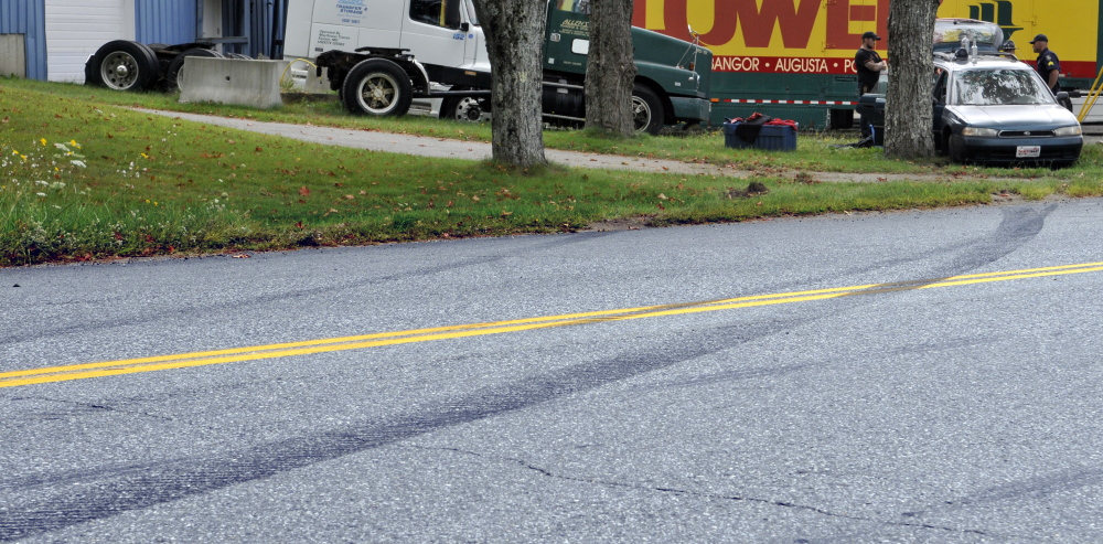 Skid marks lead the way to where tow truck drivers and State Police Troopers stand beside a crashed car on Thursday on Leighton Road in Augusta. 