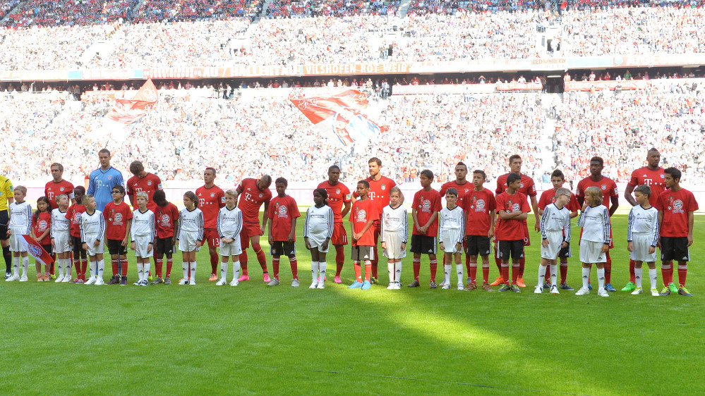 Bayern’s  players stand with refugee kids on the pitch prior to the German Bundesliga soccer match between FC Bayern Munich and FC Augsburg in the Allianz Arena in Munich on Saturday.
