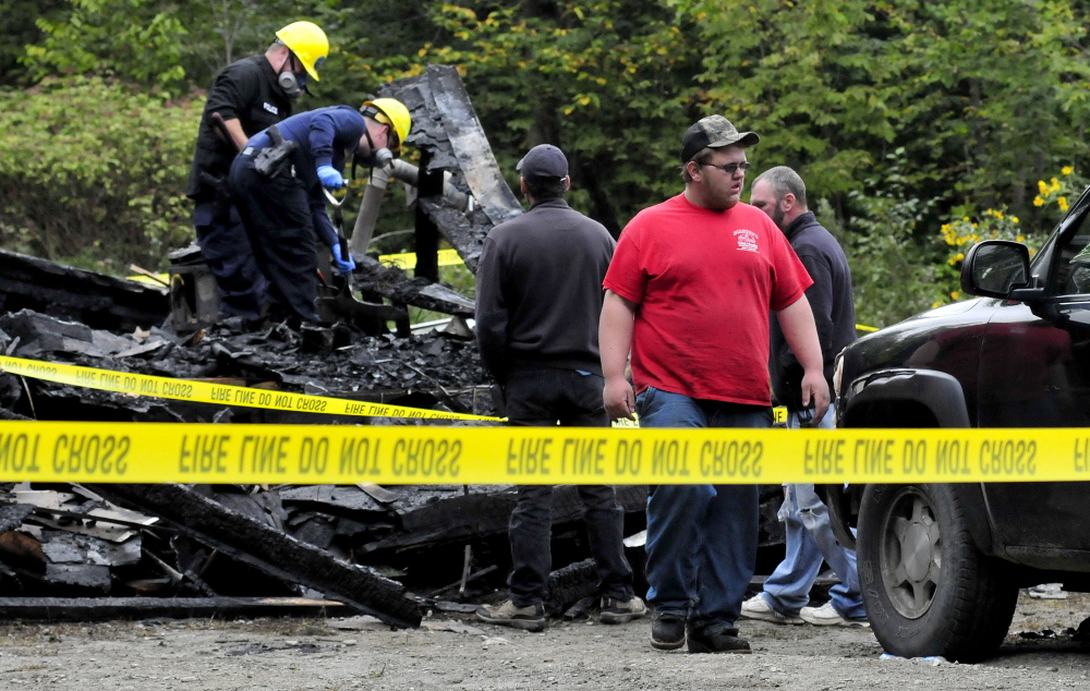 Dylan Ellis, front, walks away from the scene of a fire that destroyed his grandmother’s home where he was staying on Maple Lane in Canaan early Sunday. State fire marshal investigators John Wardwell, upper left, and Jeremy Damren look for clues to the cause in the living room area as Canaan Fire chief Troy Bowden, center, and firefighter Ed McGovern watch.