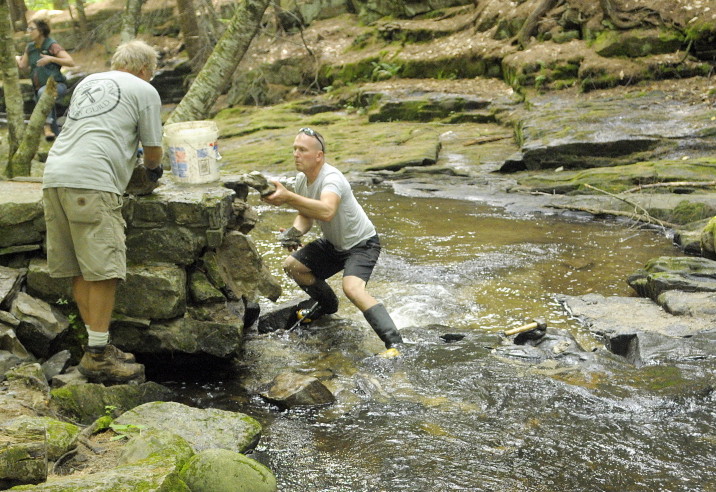 Dan Ucci, owner of Ledge Hill Creations Inc., left, and Lance Carlezon pick up fallen rocks in July after taking down a small arched bridge in Vaughan Woods in Hallowell. The bridge was built in 1900 by William Warren Vaughan and his son Sam Vaughan and local masons.