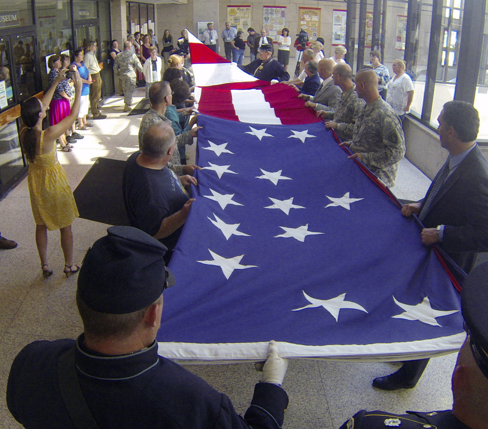 Historians and others fold an 18 by 33 foot replica of an 1860 garrison flag during a ceremony on Wednesday in the Maine State Cultural Building in the State House complex in Augusta.