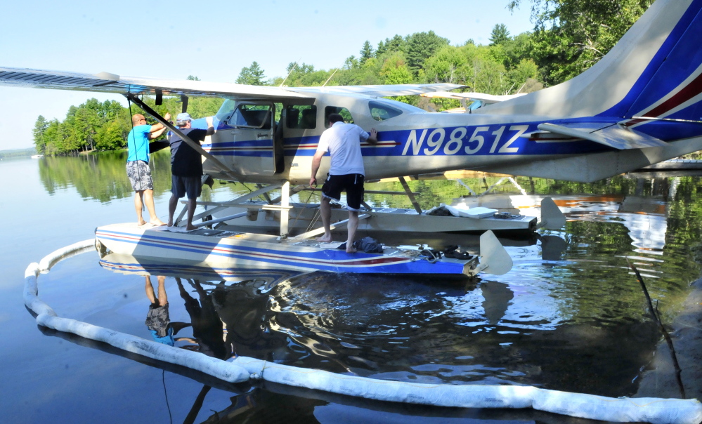 Pilot Don Stoppe, left, opens the engine compartment to his plane that was forced to land abruptly after engine failure on Wesserunsett Lake in East Madison on Thursday. Helping is passenger Perry Bryant as Stoppe’s brother and passenger Rick Stoppe gets on past oil containment pads in the water.