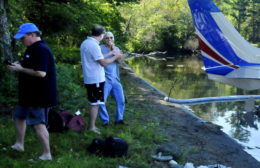 Sandy Turbyne, right, speaks with plane passenger Rick Stoppe beside the plane that was forced to land because of engine failure on Wesserunsett Lake in East Madison on Thursday. Turbyne assisted by towing the plane to shore. At left is passenger Perry Bryant.