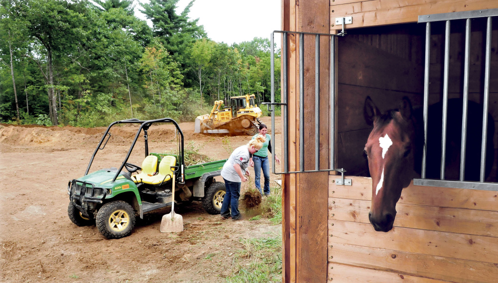 Stephanie Wrigley, left, and Milynn Phair, members of Halee Cummings’ family, pick up loose material as a bucket loader operator creates a family cemetery at the Paquette farm in Sidney. Cummings died last Friday in an all terrain accident nearby. One of her horses looks out of his stall.