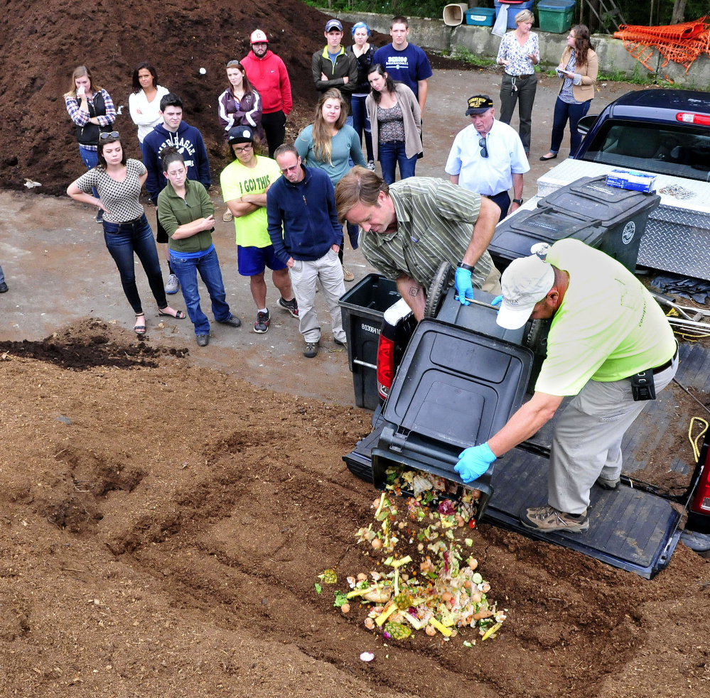Staff photo by David Leaming
University of Maine in Farmington professor Luke Kellett, left, and Mark King of the DEP pour out food waste from campus onto a pile of composting material as students watch at the Farmington Compost Cooperative site on Tuesday.