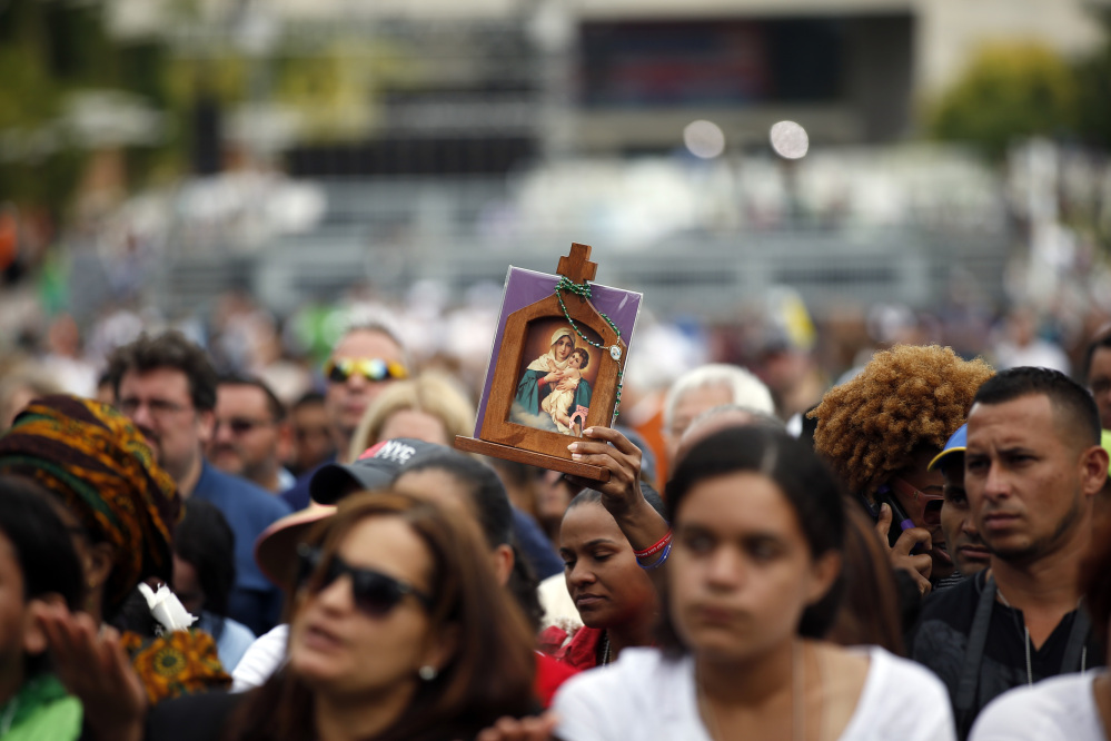A woman holds an icon as she watches Pope Francis celebrate Mass on a large video monitor as people await the arrival of the pope at Independence Hall on Saturday in Philadelphia.
