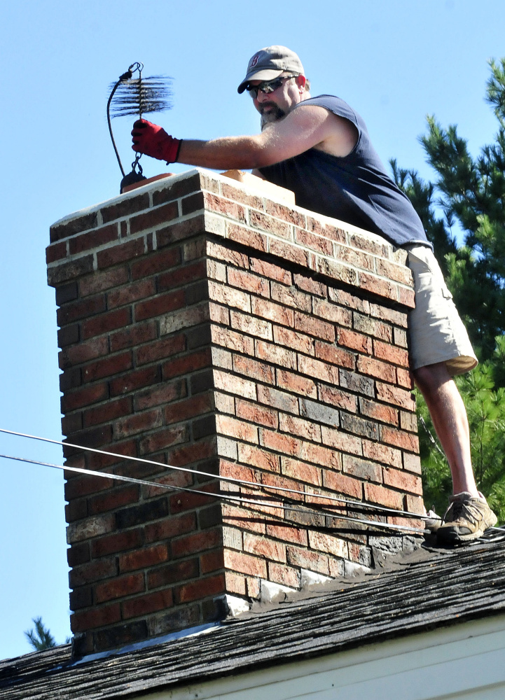 John Beane, of Complete Property Care Management Services, lifts a weighted chimney brush to clean a homeowner’s chimney on Thursday.