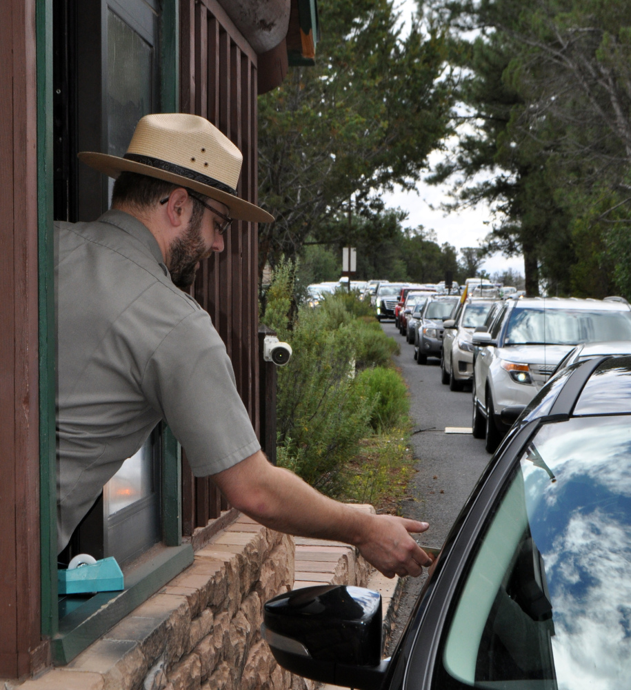 Nate Powell collects entrance fees Aug. 2 as many cars wait in line to enter Grand Canyon National Park. Visitation there is up nearly 30 percent over last year.