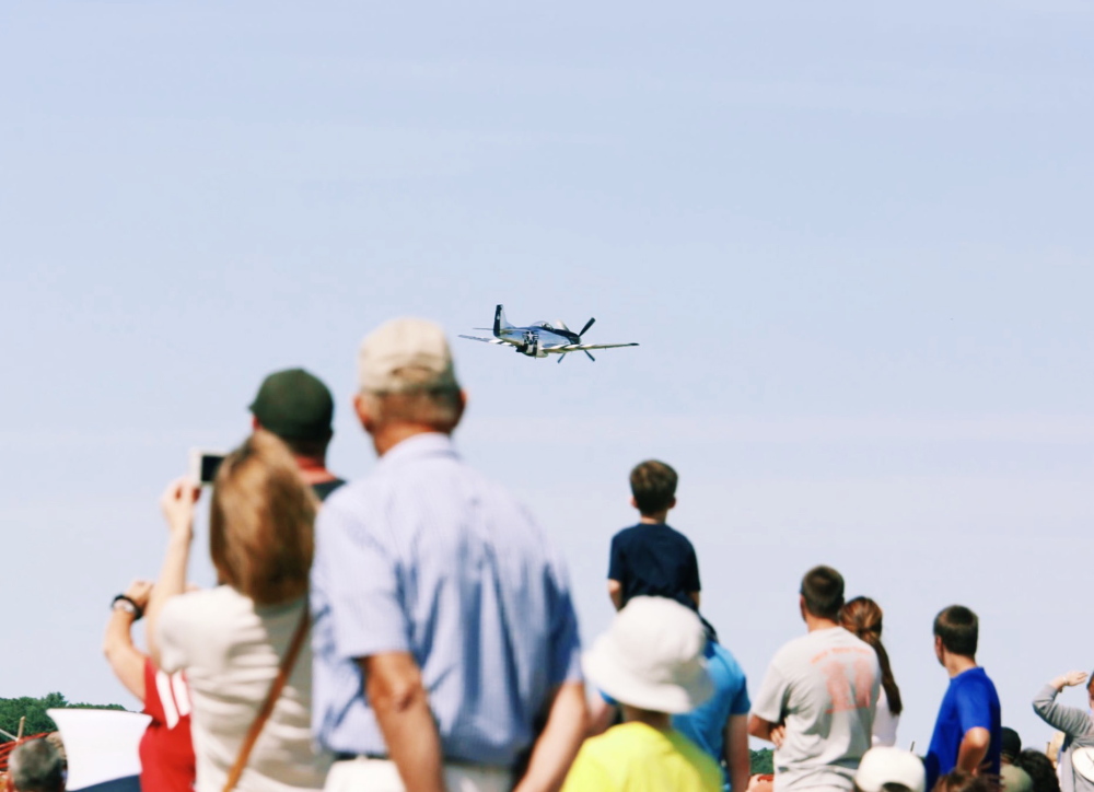 Audience members watch as a P-51 Mustang flies past during the beginning of the Airshow at Brunswick landing on Saturday.