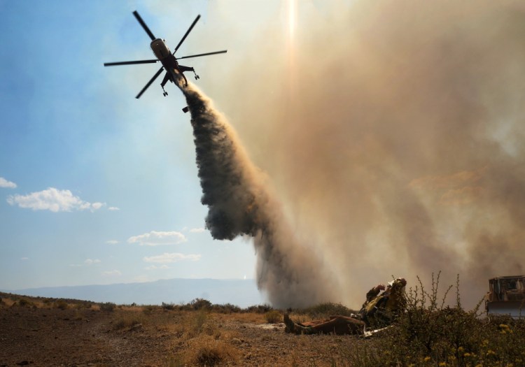 This Aug. 9, 2015 photo taken by Utah state firefighter Eli Peterson shows a firefighter watching as a helicopter makes a water drop over a fire in Owyhee County, Idaho.