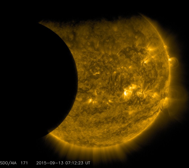The moon, left, and the Earth, top, transit the sun together on Sept. 13, as seen from the Solar Dynamics Observatory. The edge of Earth appears fuzzy because the atmosphere blocks different amounts of light at different altitudes. This image has been colorized in gold.
