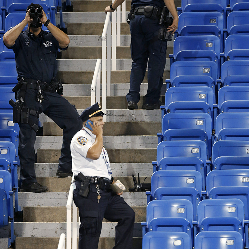 Police officers investigate an unoccupied corner of Louis Armstrong Stadium after a drone flew over the court, buzzing the players during a match between Flavia Pennetta, of Italy, and Monica Niculescu, of Romania. The drone crash-landed in the seats and can be seen to the right of the police officer on his phone.