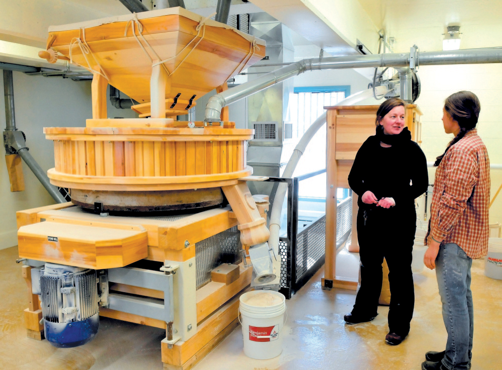 Amber Lambke, left, owner of Maine Grains, and head miller Julie Zavage discuss an order of flour being ground in the stone mill, left, at the Somerset Grist Mill in Skowhegan in 2013. A USDA grant will help help the mill buy new equipment.