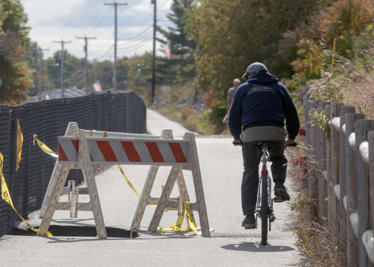 Marc Poirier looks down into the collapsed pavement as he rides past one of two washed out sections of the Kennebec River Rail Trail on Monday in Farmingdale.