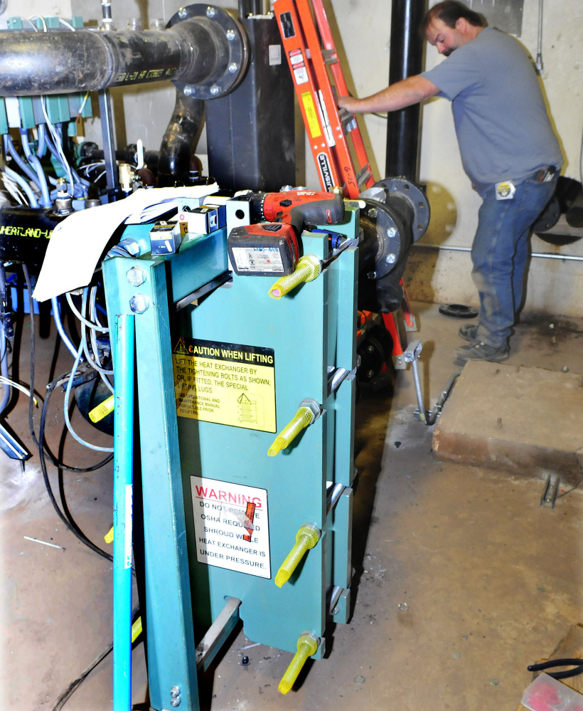 A worker installs equipment beside a compact heat exchanger for the new biomass heating system in Scott Hall dormitory at the University of Maine at Farmington. The exchanger will replace two large oil burner furnaces.