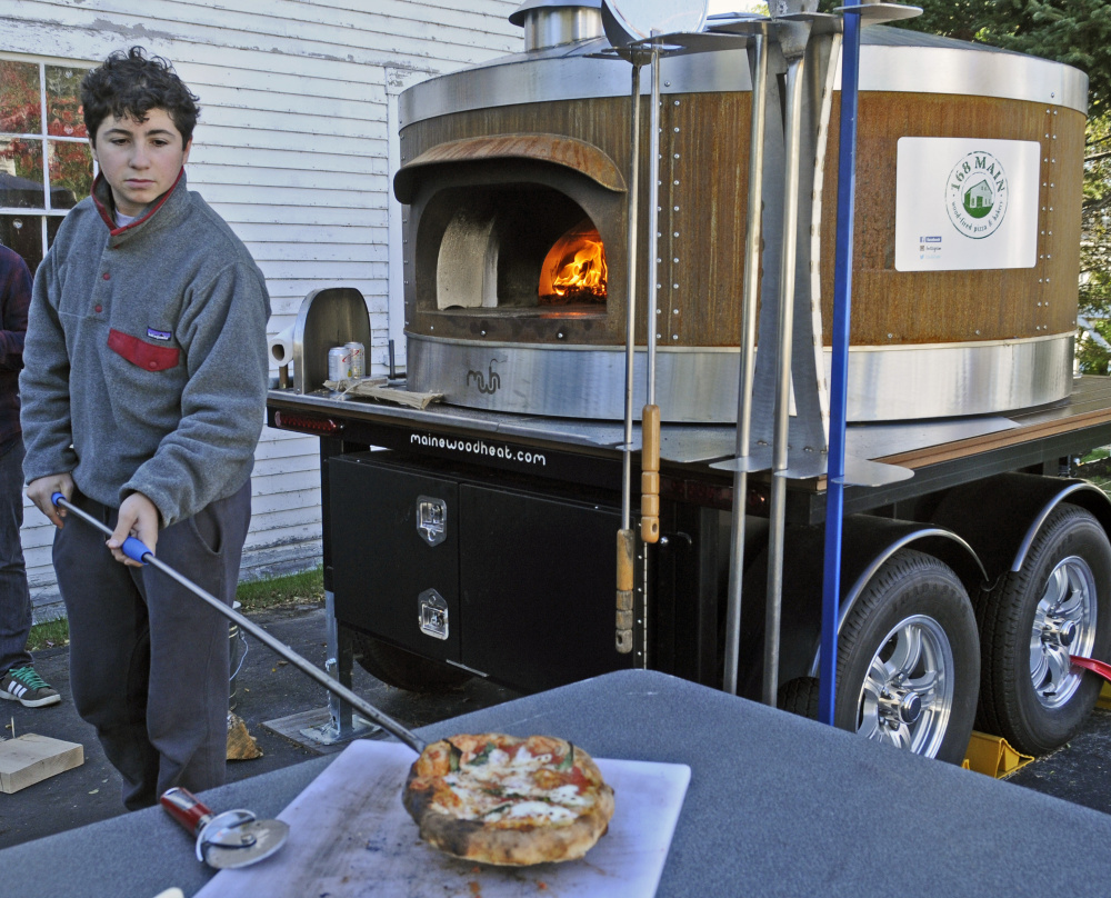 Ellis Wells pulls pizza from the wood-fired oven at 168 Main St. during harvest festivities on Saturday in Belgrade Lakes village. His uncle Sam Wells is planning to start a business selling pizzas there next summer and was offering samples during the festival.
