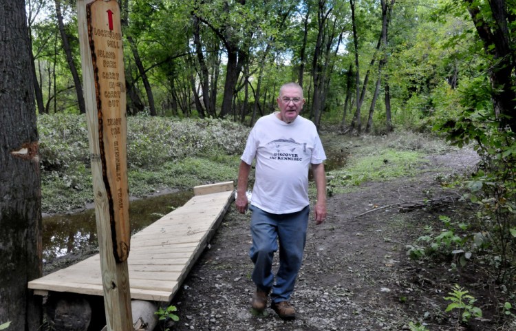 Charlie Poulin walks along the Kennebec Trail in the Lockwood Mill Island Park in Waterville recently near one of the wooden signs he made.