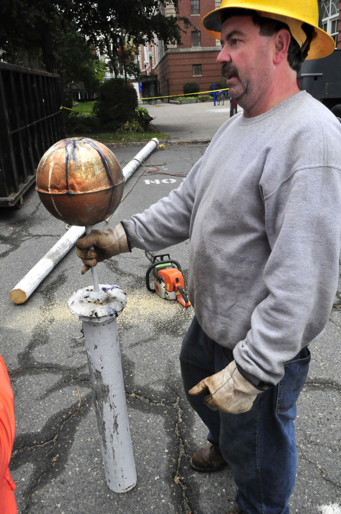 Waterville Public Works employee Mike Folsom holds the top of a 100-year-old cedar flagpole that was removed from the roof go City Hall on Tuesday. Folsom said the cut off section will likely be placed inside City Hall.