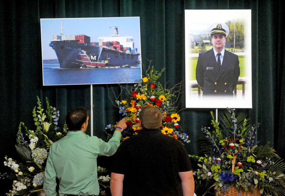 Friends and family pay their respects to a picture of Michael Holland and the cargo ship he worked on during a celebration of life at the Jay Community Building on Wednesday.