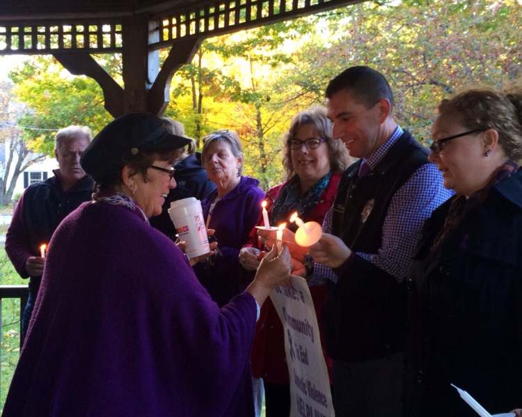 Kathleen Dumont, left, of Kennebec Valley Behavioral Health, lights a candle for Somerset County Sheriff’s Office domestic violence investigator Mike Pike, right, and others at a domestic violence awareness vigil Wednesday in Skowhegan. The vigil was part of a “speak-out” event aiming to bring awareness to domestic violence during October, which is Domestic Violence Awareness Month.